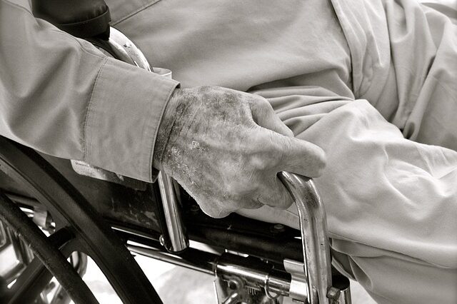 Mano di una persona anziana sul bracciolo di una sedia a rotelle, in bianco e nero